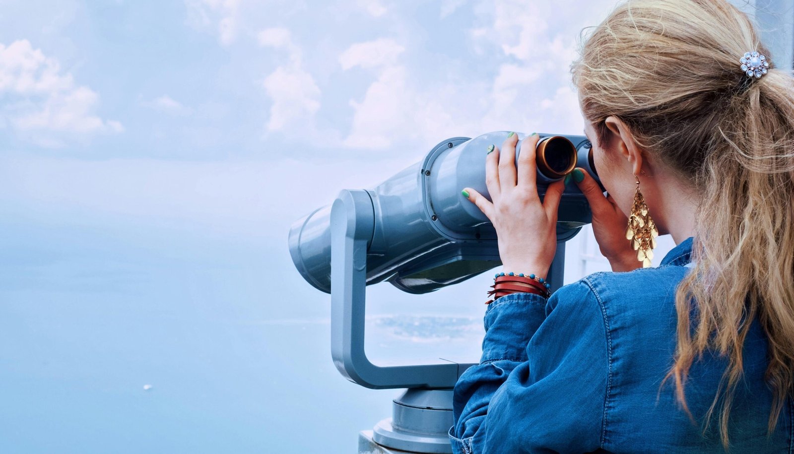 Blonde woman using a tower viewer to observe the ocean on a clear day.